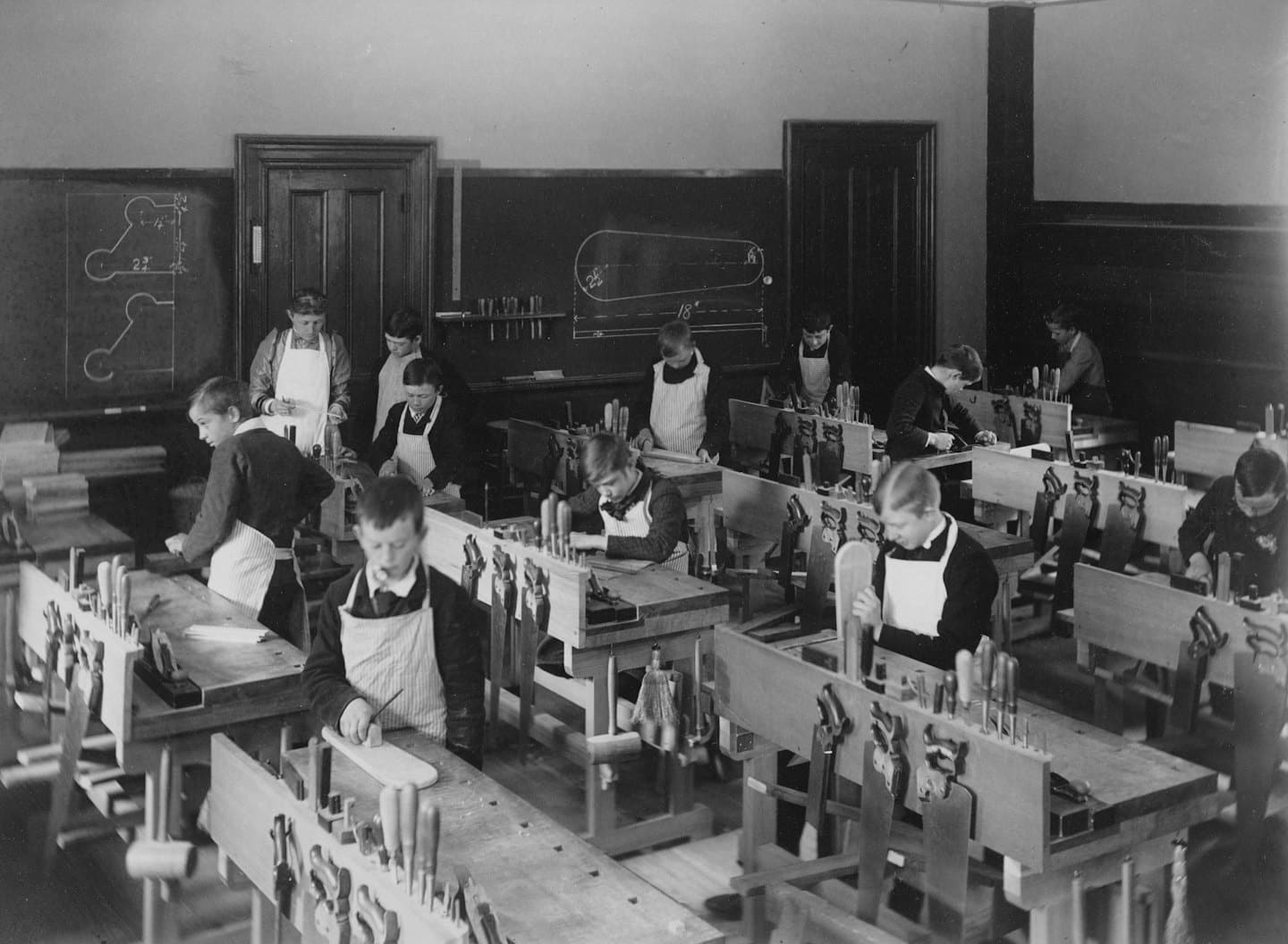 Students and their teacher work at wooden benches in a workshop.