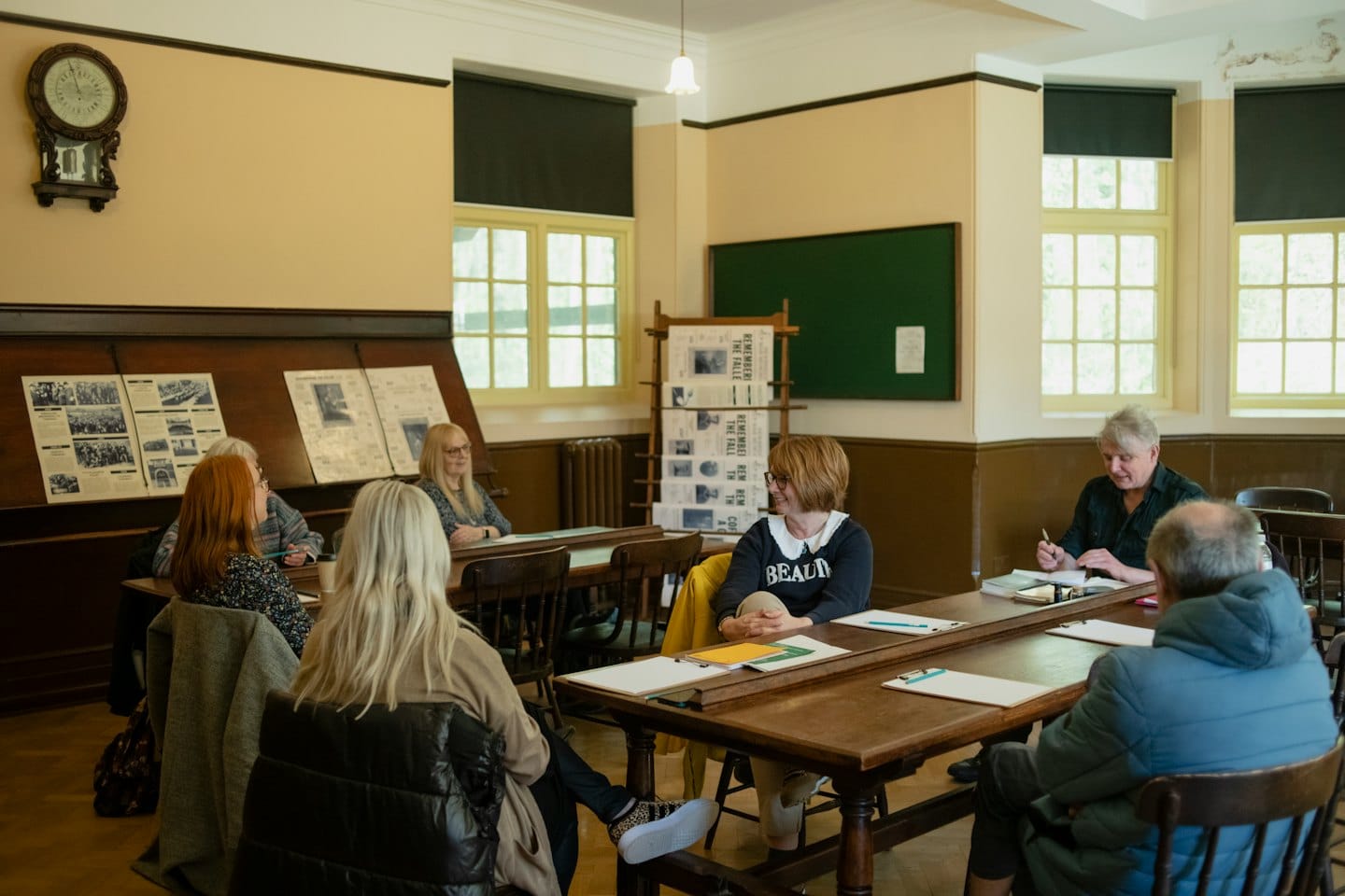 Adults discussing at wooden tables in an old-fashioned classroom.