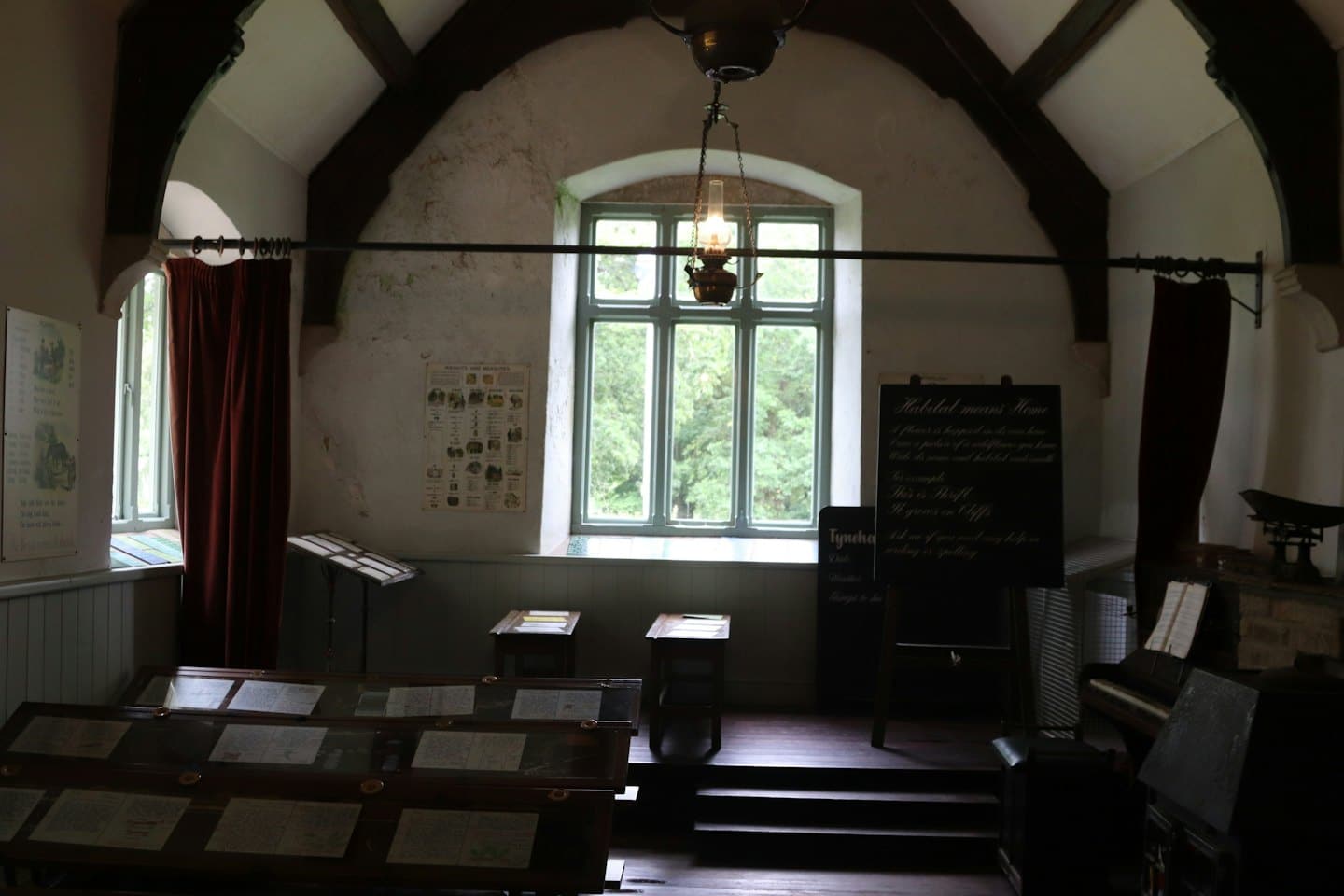 Historical schoolroom with wooden desks and blackboards under an arched ceiling.