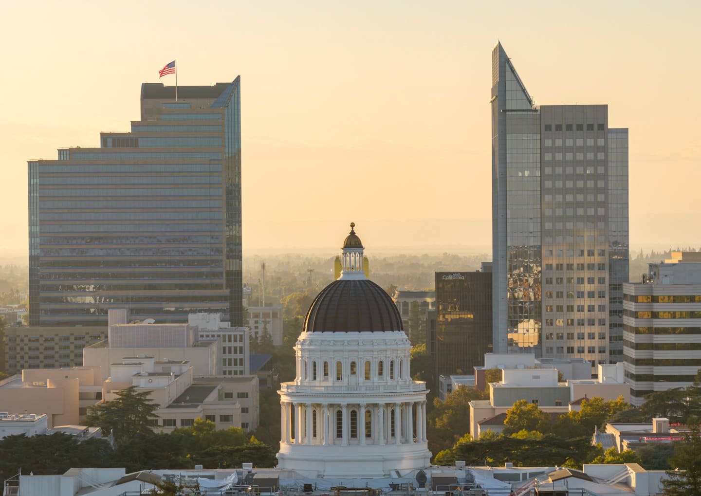 The white capitol dome stands between two tall glass skyscrapers.